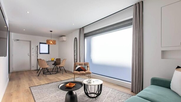 A modern living room with a sofa, a coffee table, and a dining area with chairs and a table.