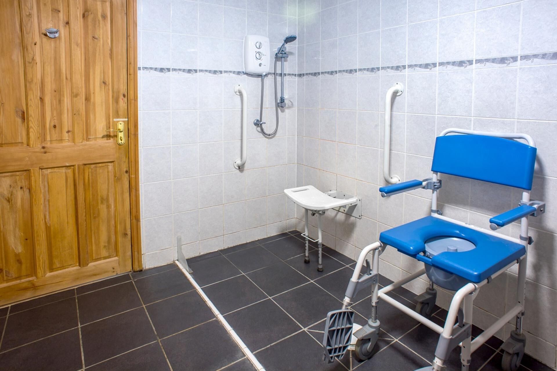 Un bagno con porta in legno, uno scafo WC azzurro, zona doccia e un piccolo lavandino.