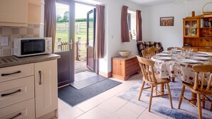 A kitchen with a microwave, wooden cabinets, a dining table set for four, and a view of a garden through open doors. - Accessible Friendly Farm Stay (Mayfield)