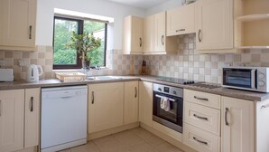 A modern kitchen with beige cabinetry, a dishwasher, an oven, a microwave, and a window with a view of greenery. - Accessible Friendly Farm Stay (Mayfield)