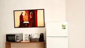 A small kitchenette with a microwave, coffee maker, and a refrigerator. There is a painting above the counter and a trash bin next to the refrigerator. - The sculptor's retreat (Niscemi)