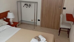 A hotel room with a bed, a chair, a small table, a lamp, and a wardrobe. - The sculptor's retreat (Niscemi)