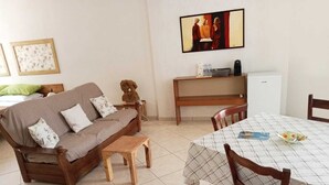 A living room with a sofa, a small wooden table, a dining table with chairs, a painting on the wall, and a refrigerator. - The sculptor's retreat (Niscemi)