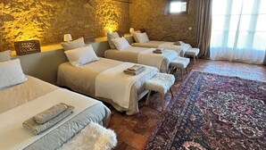 Ein Hotelzimmer mit vier nebeneinander liegenden Betten, einem großen gemusterten Teppich und einer Steinwand.