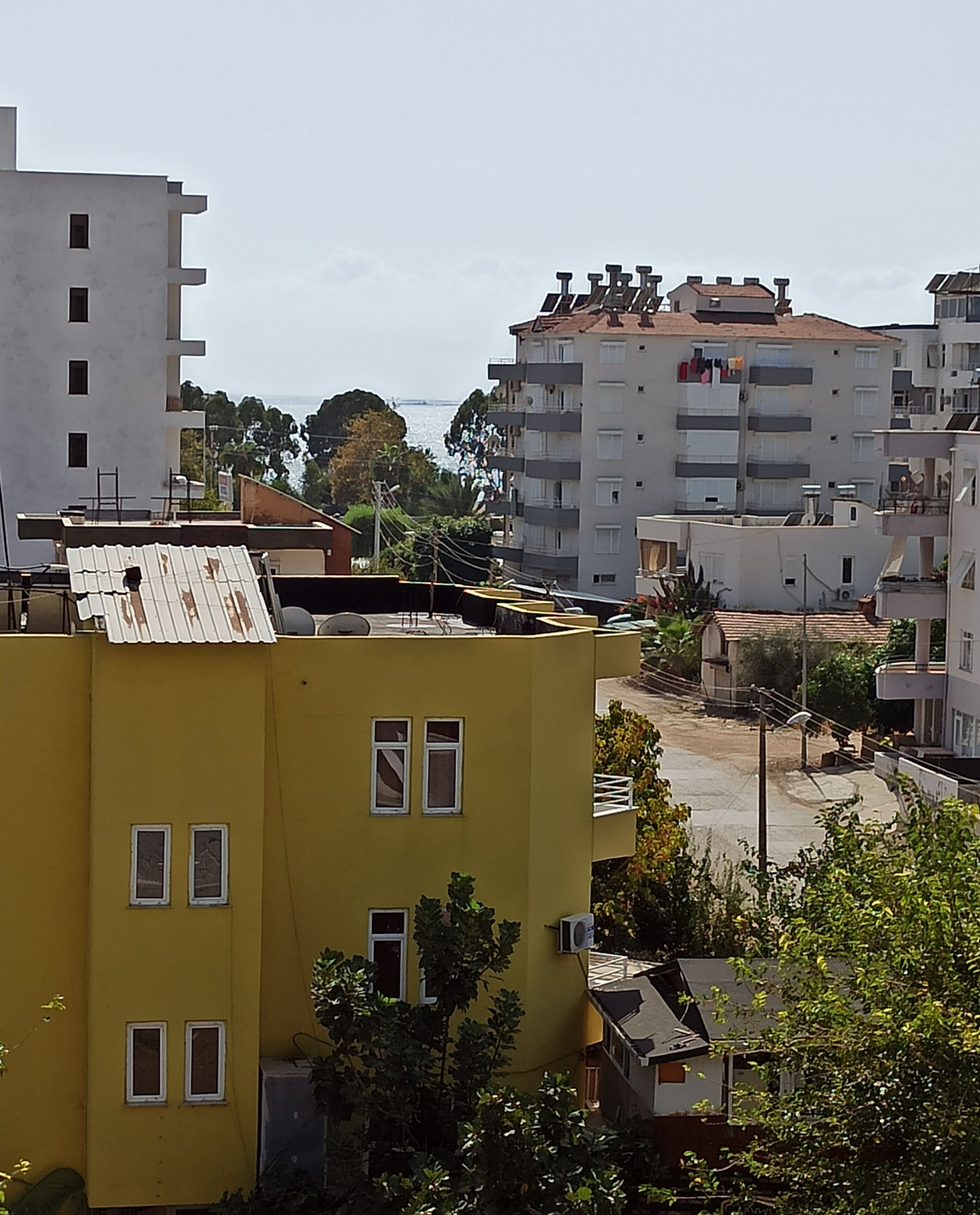 A multi-story residential building with balconies, a flat roof, and a visible water body in the background.