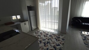 A modern kitchen with a built-in oven, a refrigerator, and a window with sheer curtains. - Şahiner Apart Otel (Finike)