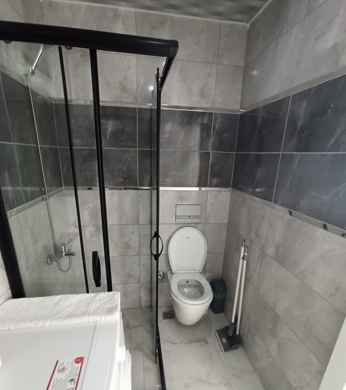 A bathroom with a glass-enclosed shower, a toilet, and a trash bin.