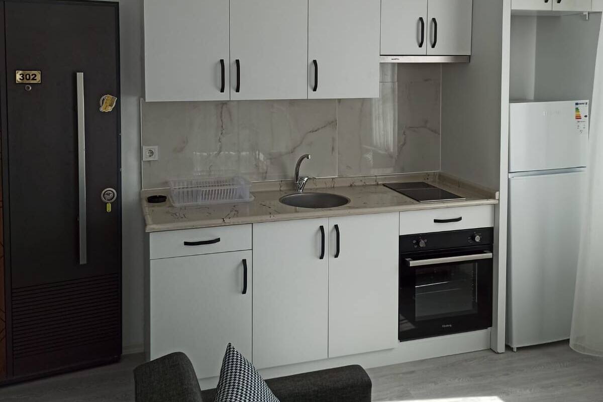Eine moderne Küche mit weißen Schränken, einem schwarzen Kühlschrank, einem eingebauten Backofen und einer Marmorarbeitsplatte.