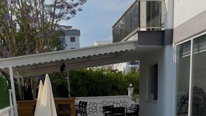 A swimming pool with lounge chairs and umbrellas, a wet floor sign, and a patio area with outdoor furniture. - Şahiner Apart Otel (Finike)