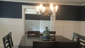 Een eetkamer met een donker houten tafel en stoelen, een kroonluchter en een vaas op tafel.