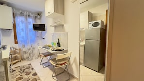 A compact kitchen with a refrigerator, microwave, and a small dining area with a table and chairs. - Ca de la Corona - Camera in Cima by Ca-sa Check (Chioggia)
