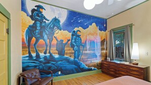 Un dormitori amb un mural d'exploradors espacials, un taulell de fusta, un llit i una cadira d'oscillació.