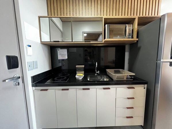 A compact kitchen with a black countertop, white cabinets, a built-in microwave, and a stainless steel refrigerator. - Edifício New Time 1215 (Maceió)