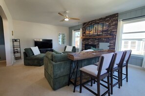 A living room with a fireplace, a television, and a dining area with chairs. - Big home - walk to the beach - First year offered (Ludington)