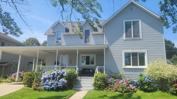 A two-story house with a porch, a front door, and a small front yard with flowers.