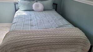 A bed with a quilted bedspread and a knitted throw blanket.