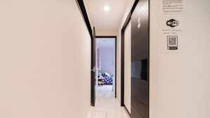 A hallway leading to a bedroom with a bed, a nightstand, and a small table. There is a Wi-Fi sign on the wall and a QR code for scanning. - Upscale Sumida Retreat: Skytree Views, Workspaces & Premium Decor, 6 people (Sumida City)