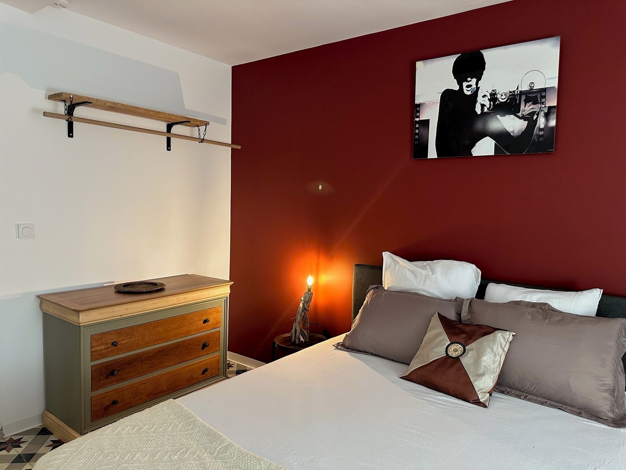 A bedroom with a bed, dresser, and a wall-mounted shelf.