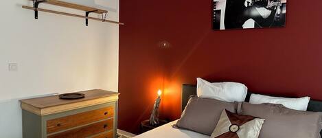 A bedroom with a bed, dresser, and a wall-mounted shelf.