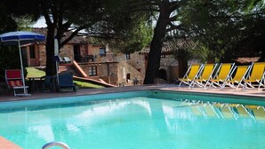 A swimming pool with clear water, surrounded by lounge chairs and a stone building with a tiled roof.
