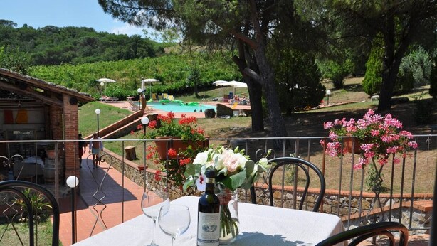 An outdoor dining area with a table set for two, a bottle of wine, and a vase of flowers.