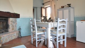 A dining area with a stone fireplace, white chairs, a table, and a white refrigerator.