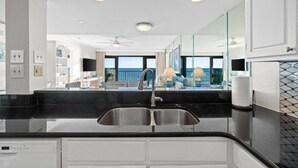 A modern kitchen with a black countertop, stainless steel sink, and white cabinetry. - Fall Deals + Snowbird Rates | Gulf Front Beach Escape (Panama City Beach)