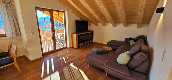 A living room with a wooden ceiling, a sofa, a television, and a sliding glass door leading to an outdoor deck.