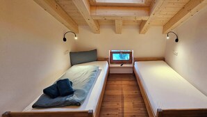 A small, cozy room with two single beds, wooden beams on the ceiling, and a small TV on a nightstand. - Apartment Hipp No. 10 - 67m² new building on the top floor with balcony, mountain and castle view Top location (Halblech)