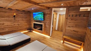 A cozy room with wooden walls, a bed, a fireplace, and a TV on the wall. - Apartment Hipp No. 10 - 67m² new building on the top floor with balcony, mountain and castle view Top location (Halblech)