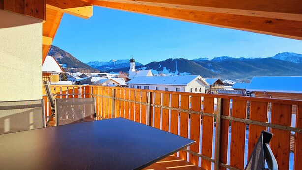 A balcony with a table and chairs, overlooking a town with buildings and mountains in the background. - Apartment Hipp No. 10 - 67m² new building on the top floor with balcony, mountain and castle view Top location (Halblech)