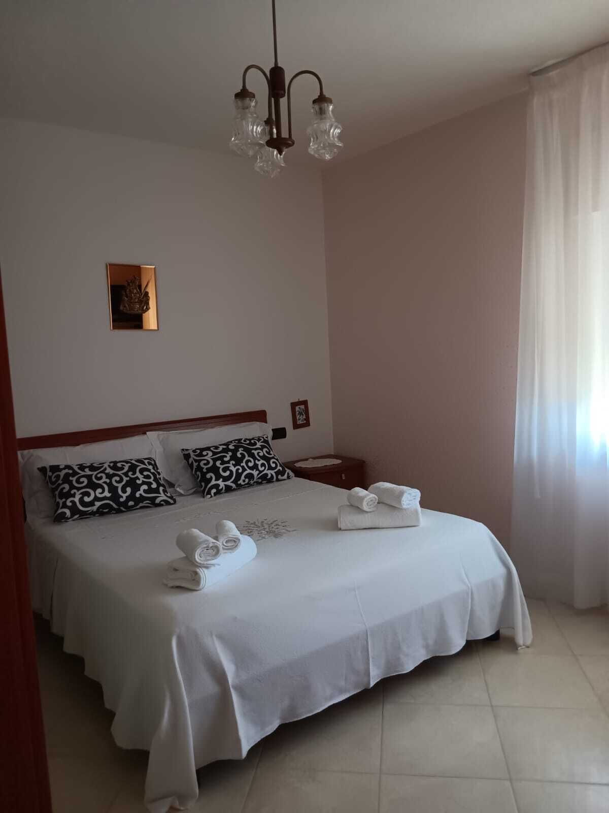Una cama bien hecha con sábanas blancas y almohadas estampadas en negro, una mesita de noche con una lámpara y un candelabro en el techo.