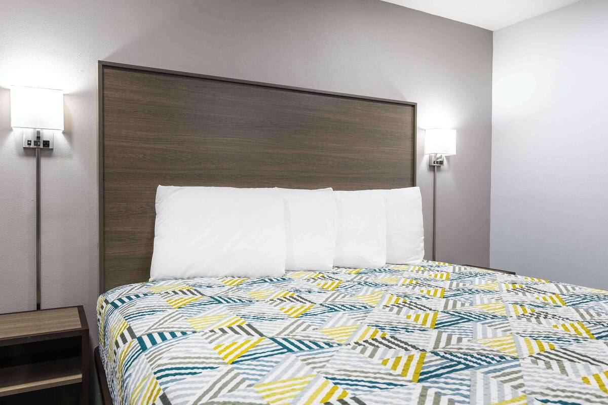 Una habitación de hotel con una cama, dos lámparas de noche y una mesita de noche.