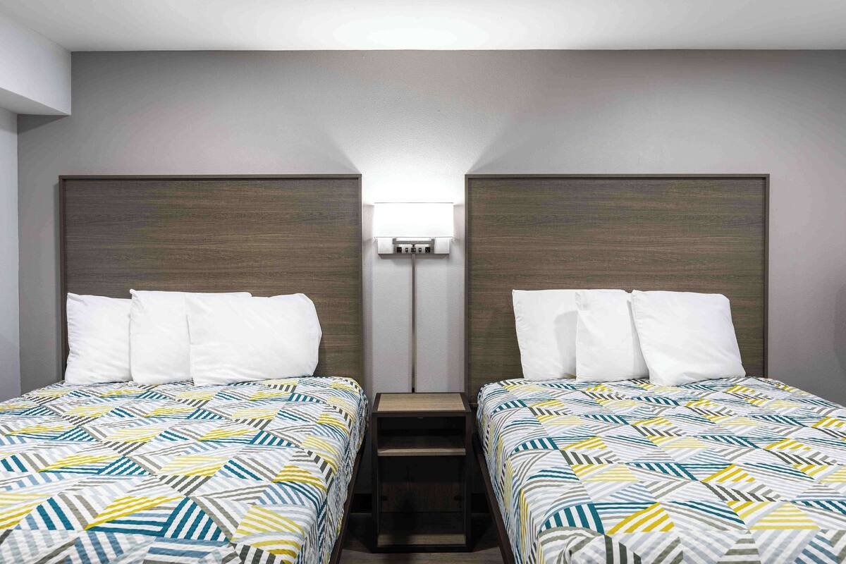 Una habitación de hotel con dos camas individuales, una mesita de noche entre ellas y una lámpara fijada a la pared.