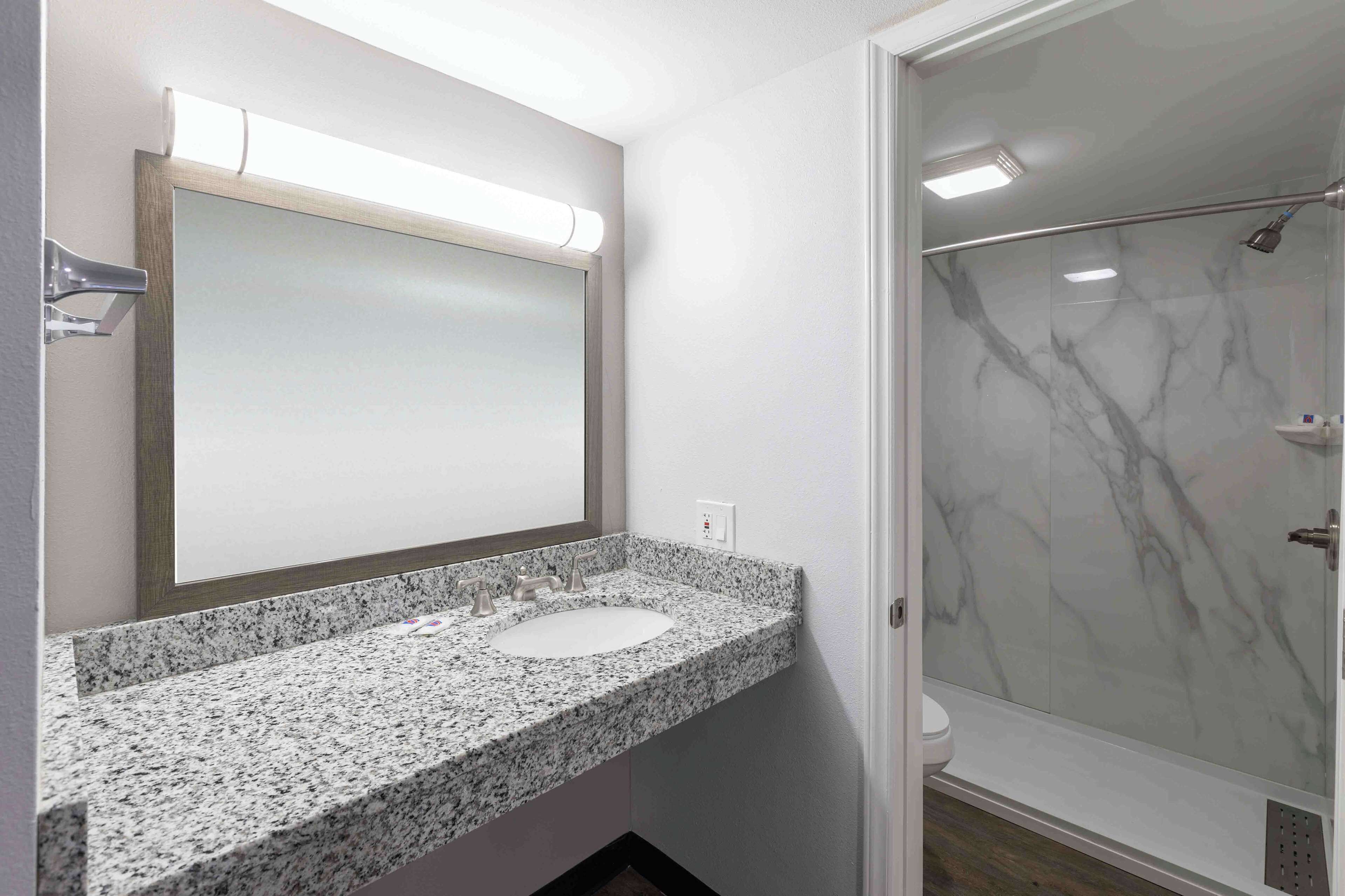 A bathroom with a granite countertop sink, a mirror, and a glass shower enclosure.