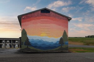 Un edificio con un mural de un atardecer sobre montañas y árboles.