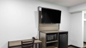 A compact room with a flat-screen TV mounted on the wall, a small wooden desk with a chair, and a built-in refrigerator. - Motel 6 Hickory, NC (Hickory)
