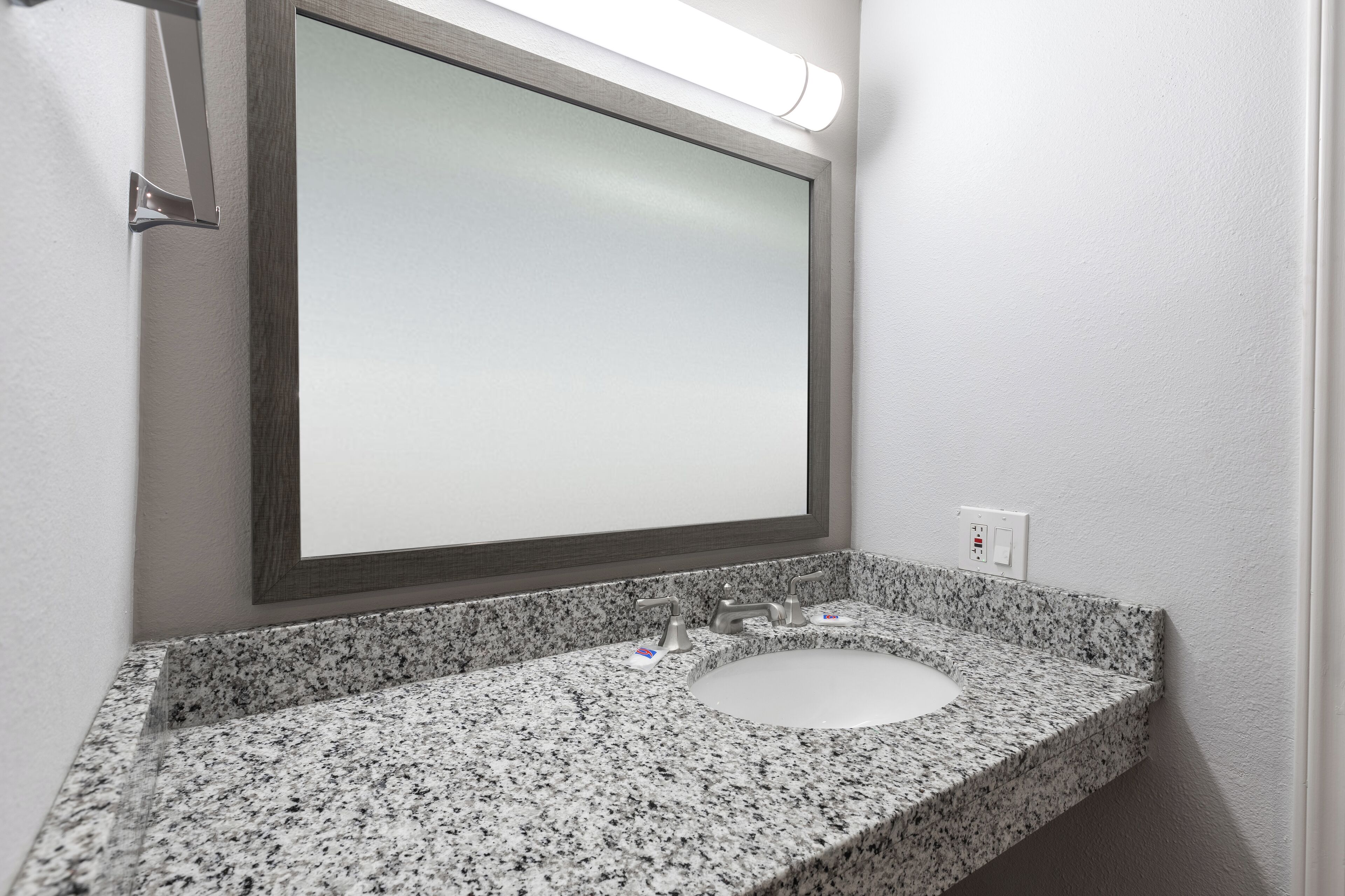 A bathroom with a granite countertop, a white sink, and a mirror with a wooden frame.