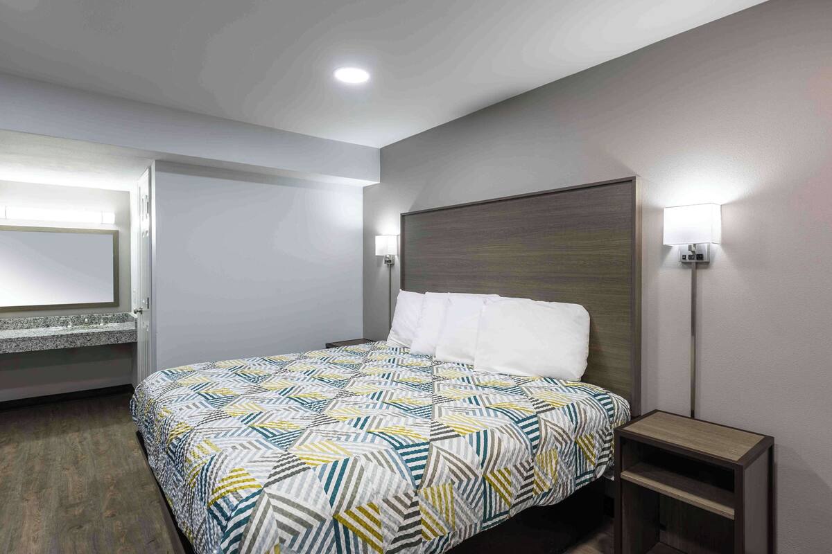 Una habitación de hotel moderna con una cama grande, una mesita de noche, un espejo y una lámpara de pared.