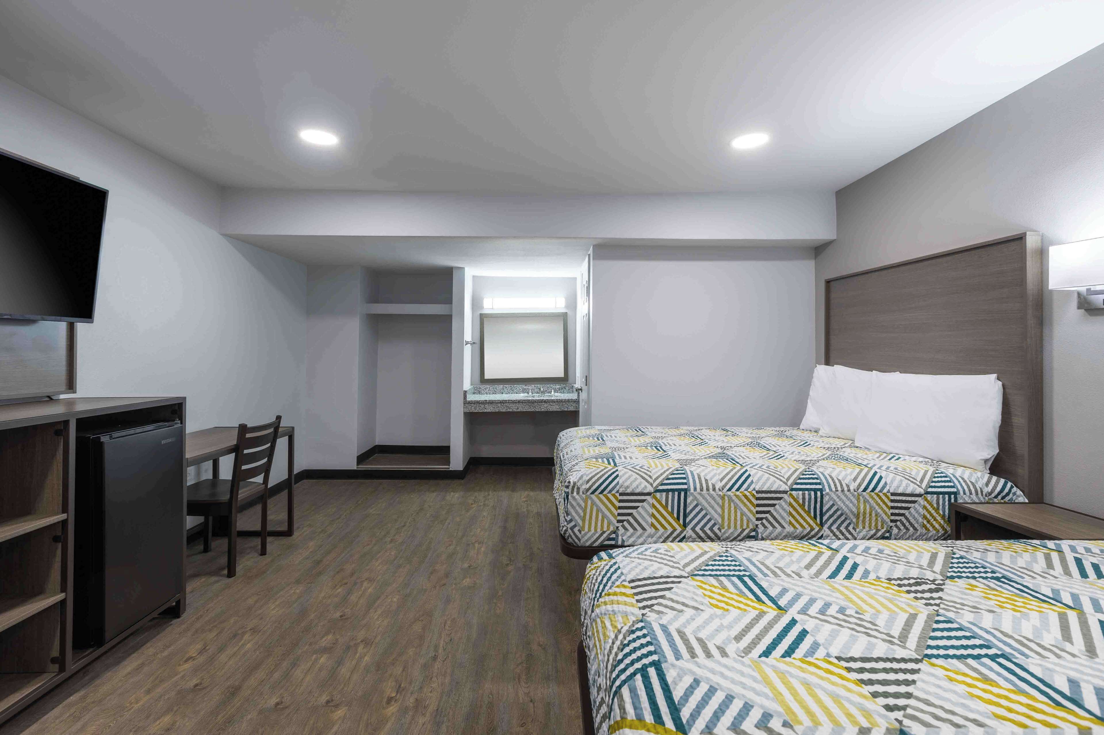 A hotel room with two beds, a desk, a chair, a TV, and a wardrobe.