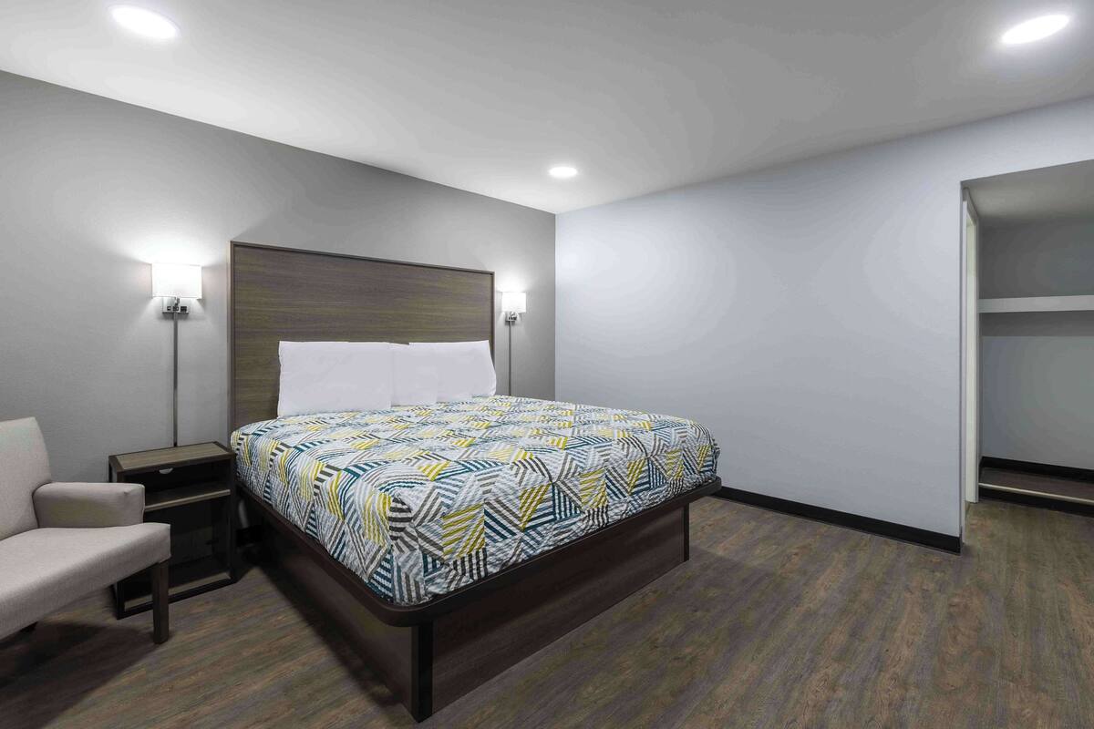 Una habitación de hotel con cama, mesita de noche, silla y armario.