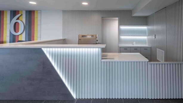 A modern reception area with a large number '6' on the wall, a reception desk, and a built-in coffee machine. - Motel 6 Hickory, NC (Hickory)