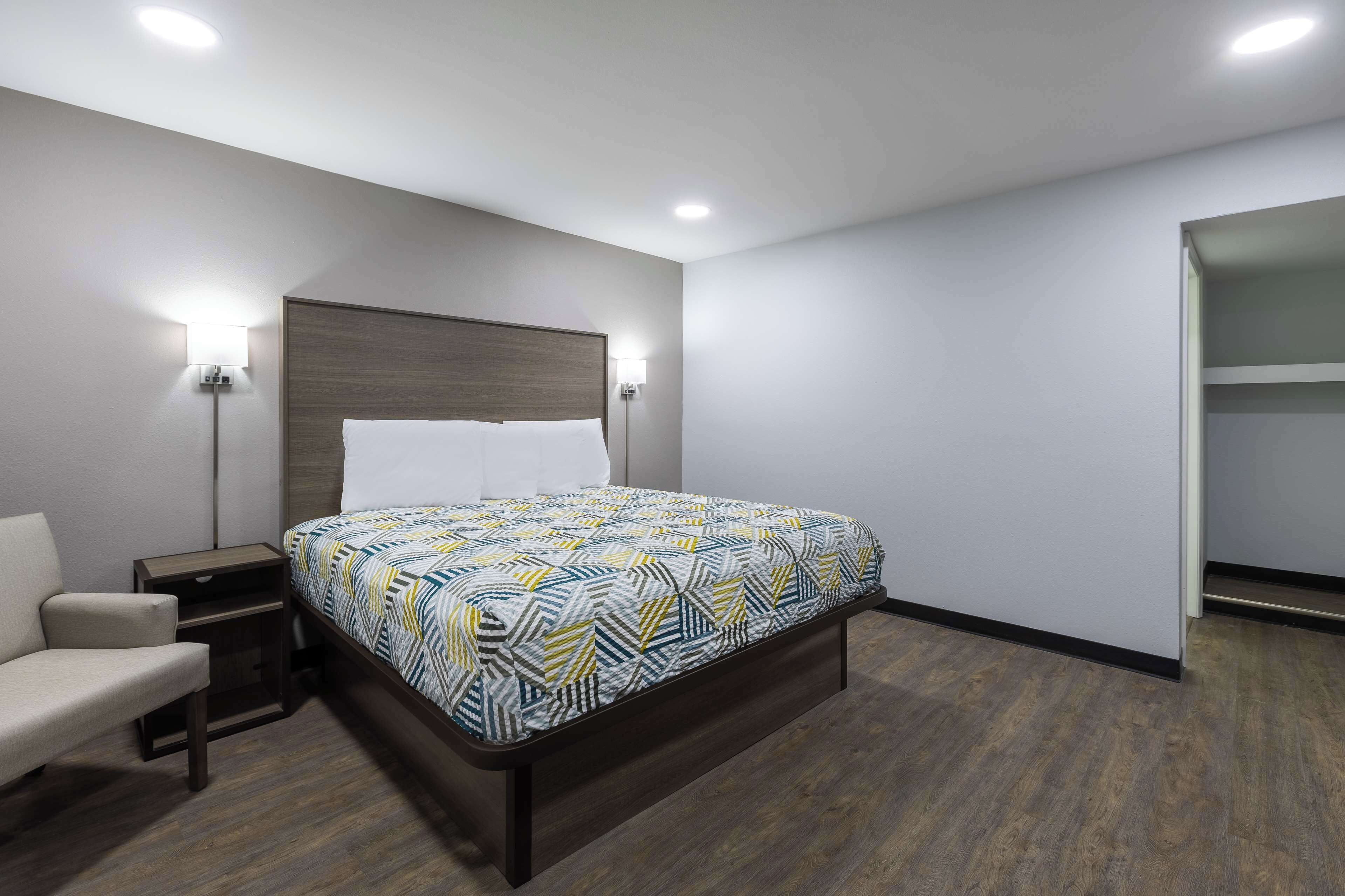 A hotel room with a bed, bedside table, lamp, and a chair.