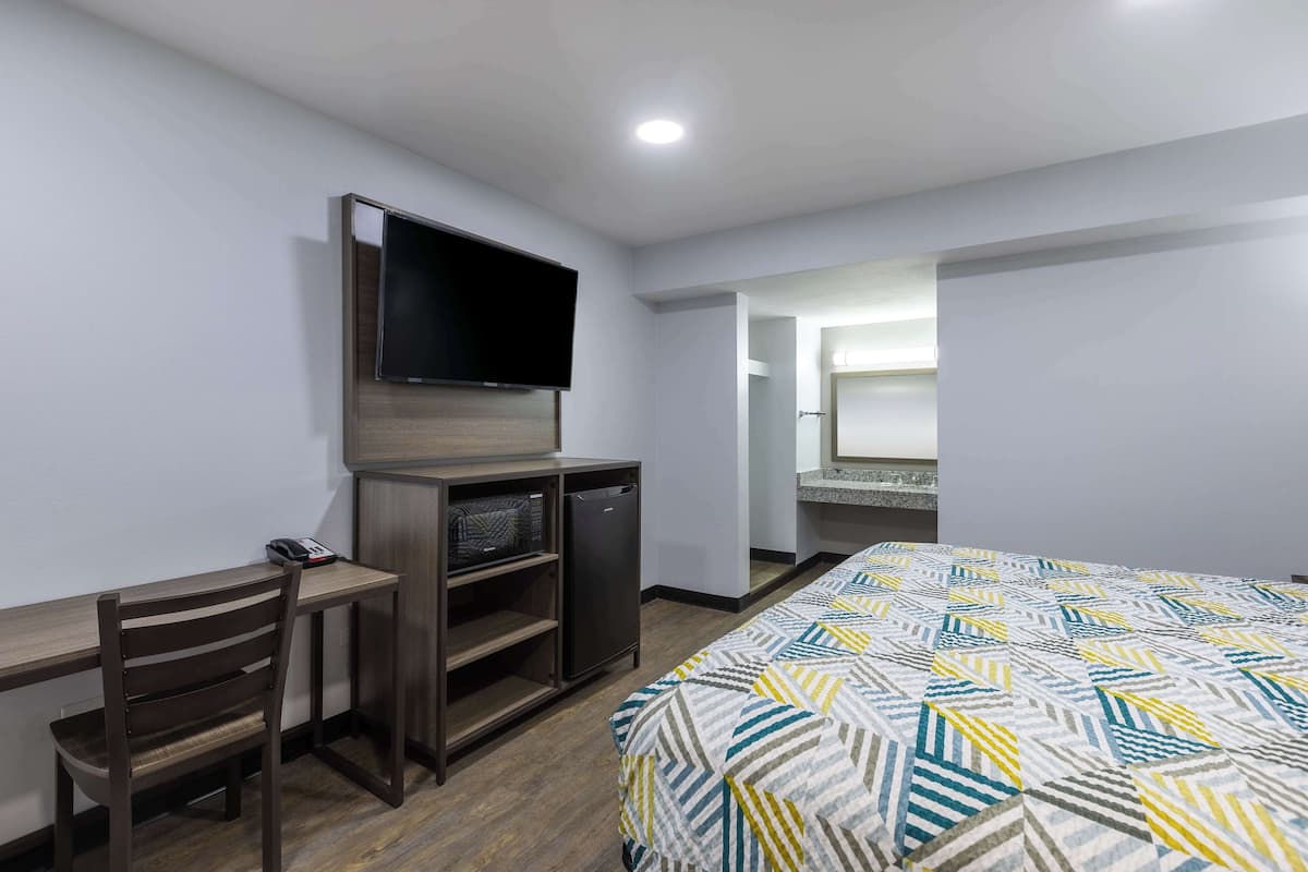Habitació d'hotel amb llit, escriptori amb cadira, televisió i nevera petita.