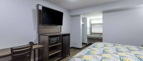Habitación de hotel con cama, escritorio con silla, televisor y refrigerador pequeño.