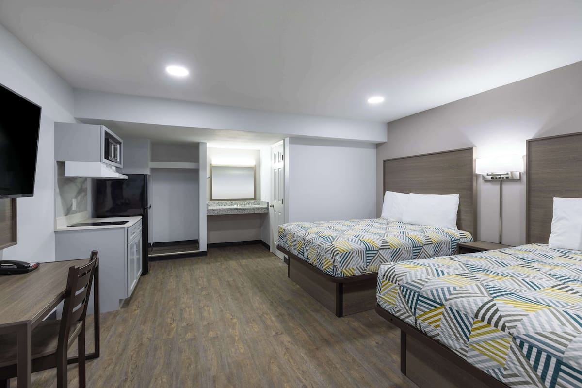 Habitació d'hotel compacta amb cuina americana, dos llits amb roba de llit estampada, un escriptori i una cadira.