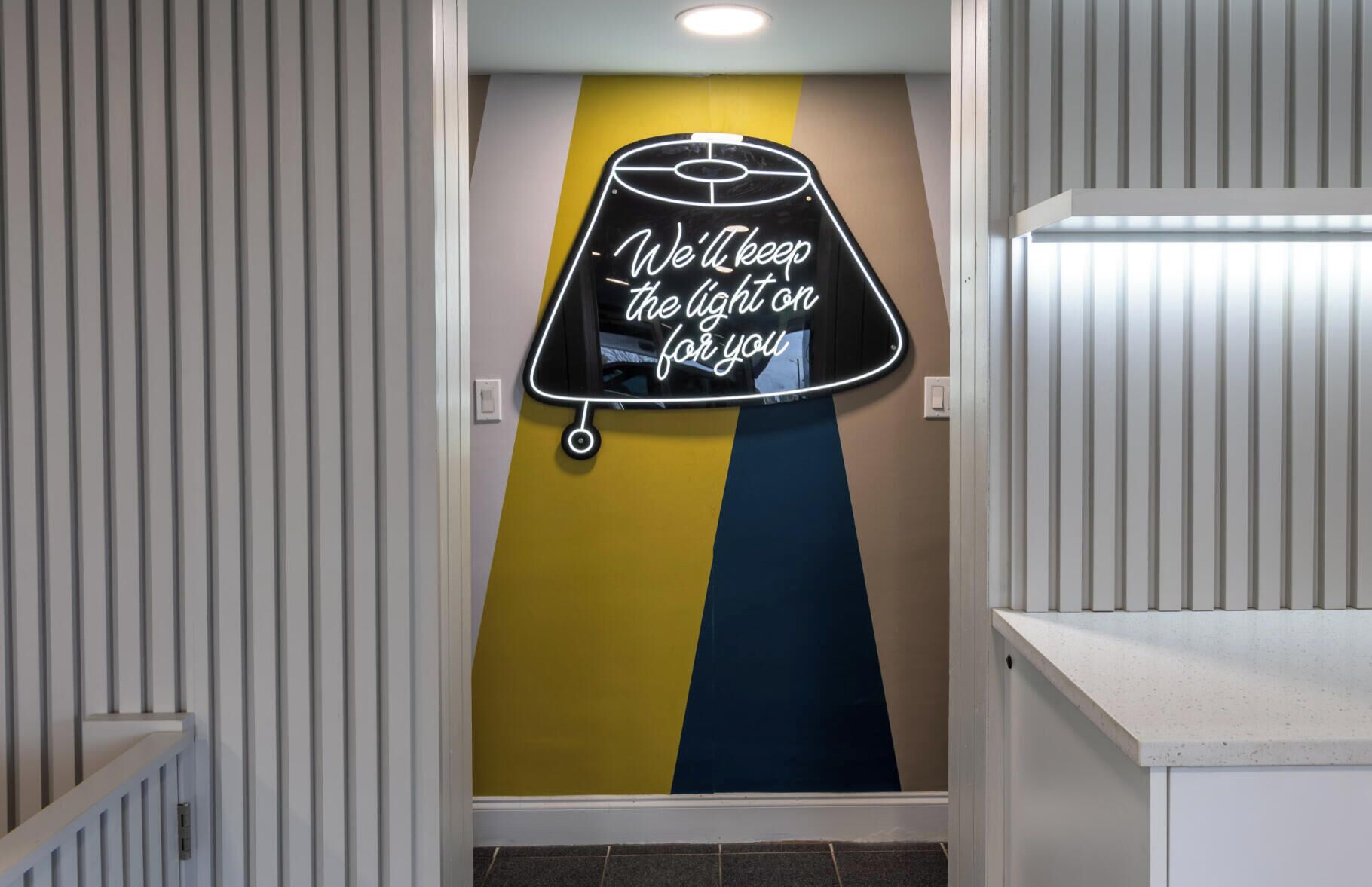 A hallway with a neon sign on the wall, a staircase, and a door.