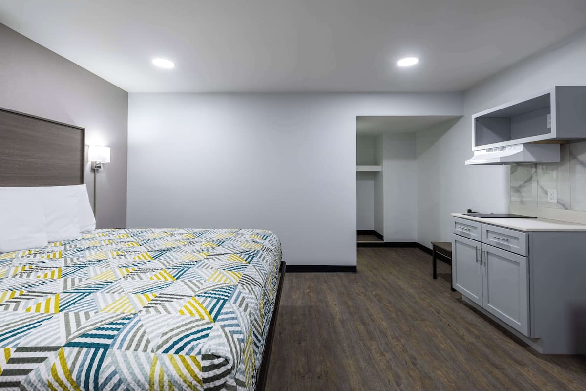 Habitació d'hotel amb llit, petita cuina i bany visible per una porta oberta.