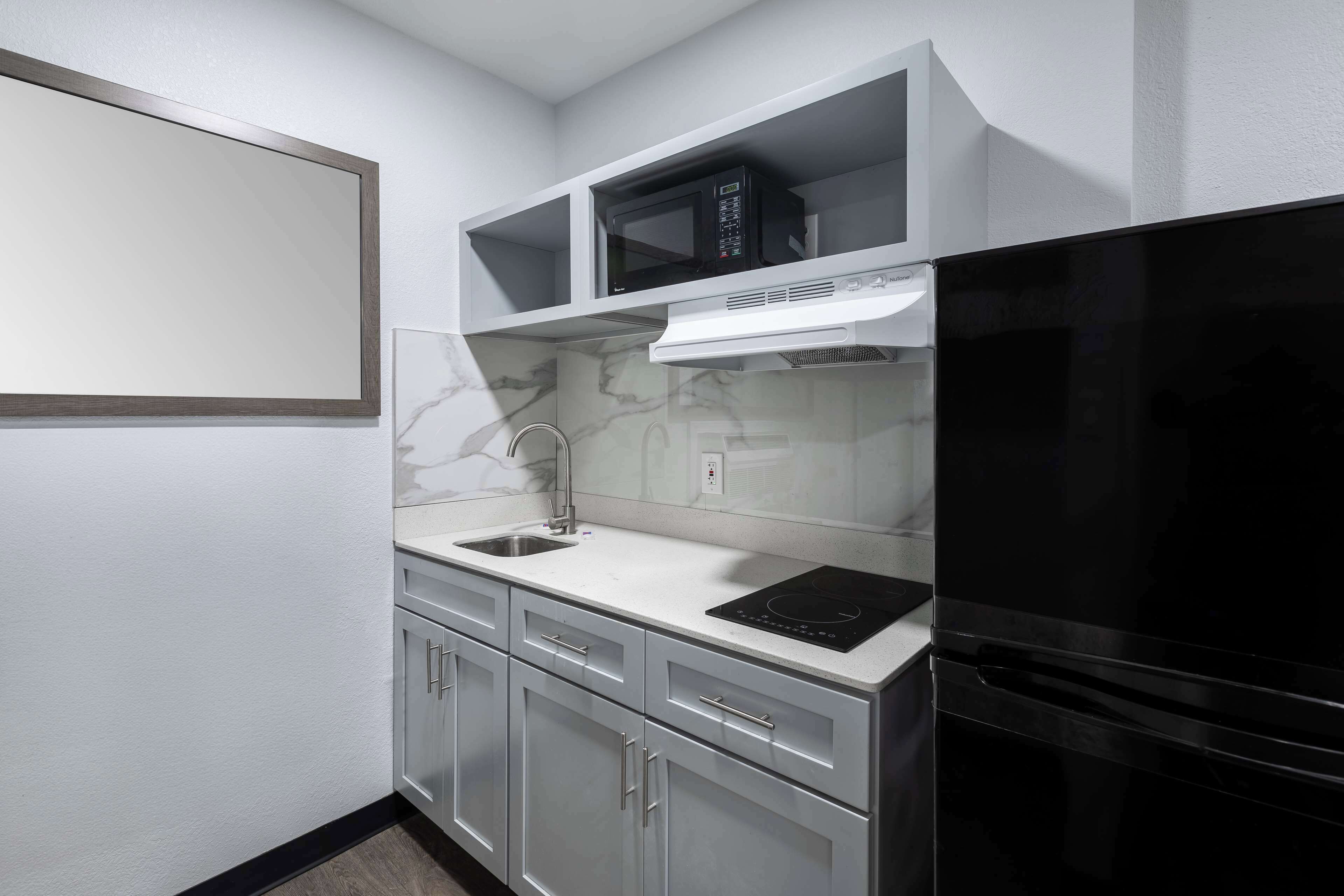 A compact kitchen with a black refrigerator, white cabinets, a microwave, and a built-in oven.