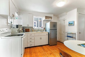 A kitchen with white cabinets, a stainless steel refrigerator, a microwave, and a wooden floor.